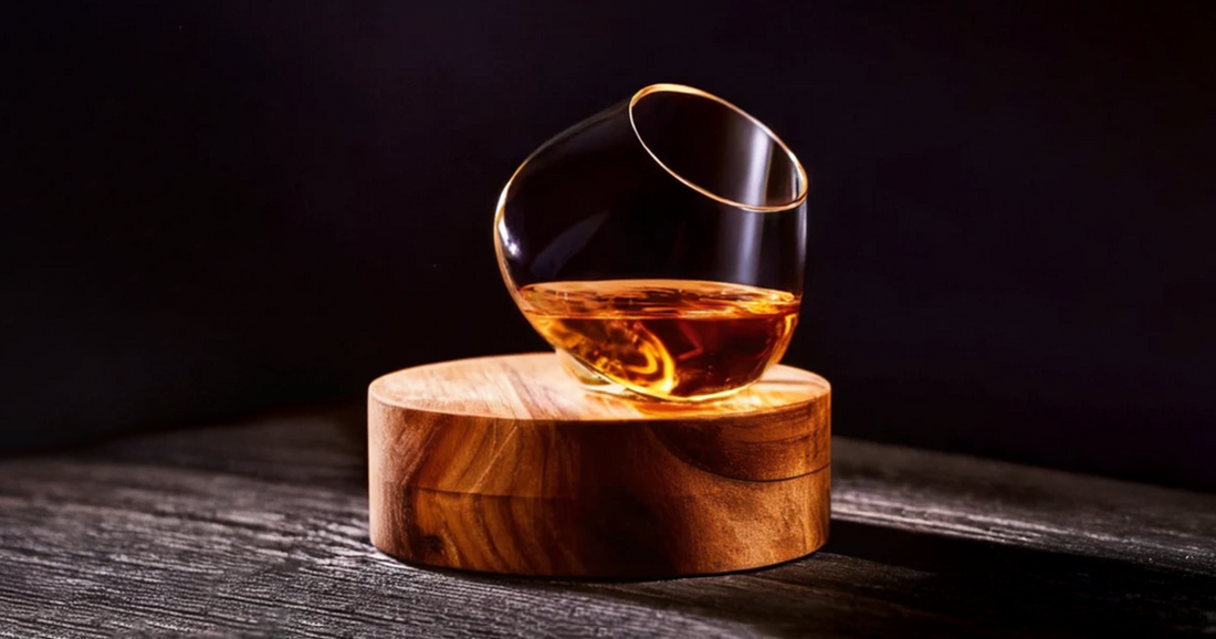 Aequilibrium Spirit Glass by Audacem filled with whisky, placed on a wooden coaster in soft light