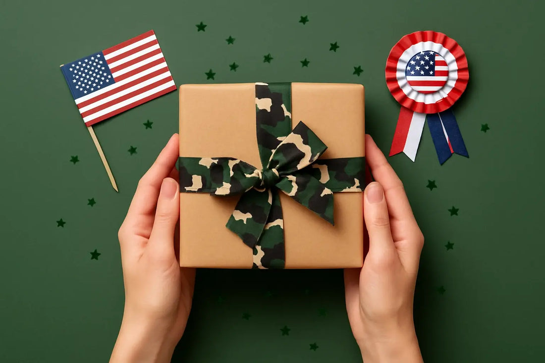 Hands holding a gift wrapped in brown paper with a camouflage ribbon, on a green background with an American flag and a USA-themed rosette in the background.