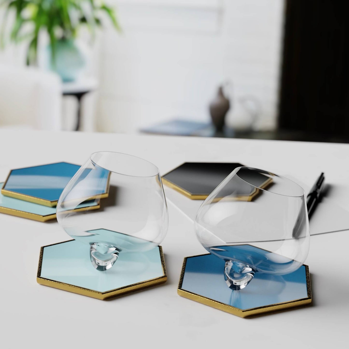 Aequilibrium glasses and hexagonal ceramic coasters by Audacem displayed on a white table.