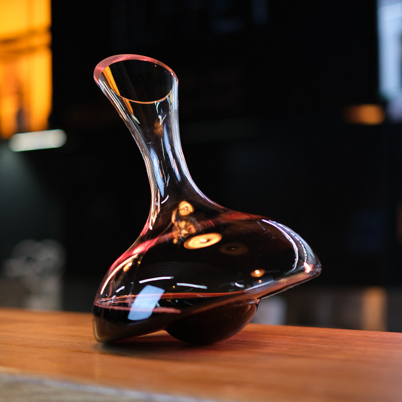 Aequilibrium crystal wine decanter with red wine, showcased on a wooden surface against a modern dark interior.