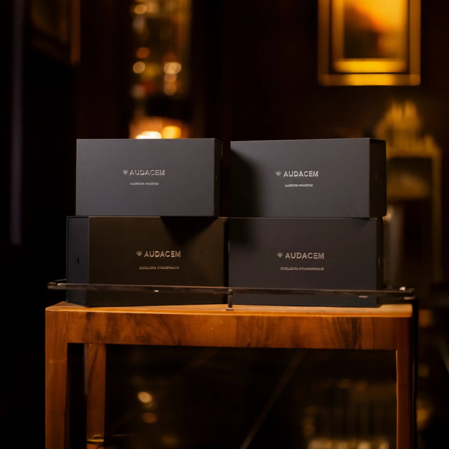 Four black boxes with 'AUDACEM' branding on a wooden table in a dimly lit room.