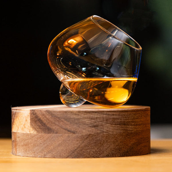 Aequilibrium Whisky Glass by Audacem – hand-blown tilted glass resting on a wooden base with amber whisky inside, designed to enhance aroma and balance.
