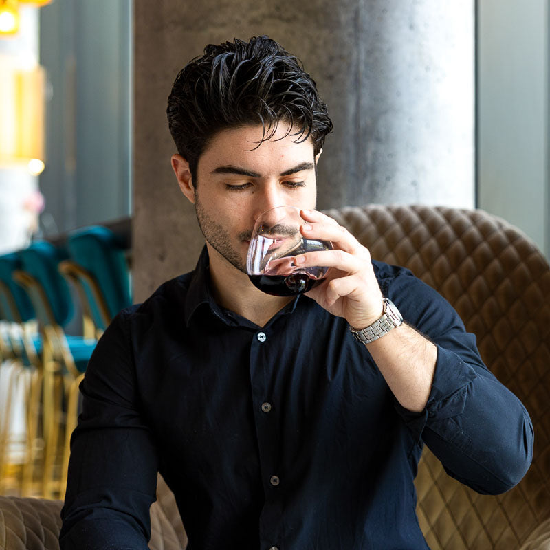 Man sipping red wine from Aequilibrium glass in modern lounge setting.