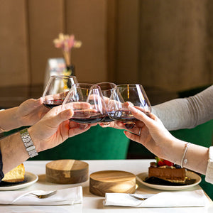 Group toasting with Aequilibrium crystal glasses filled with red wine by Audacem with wooden coasters, during a dinner