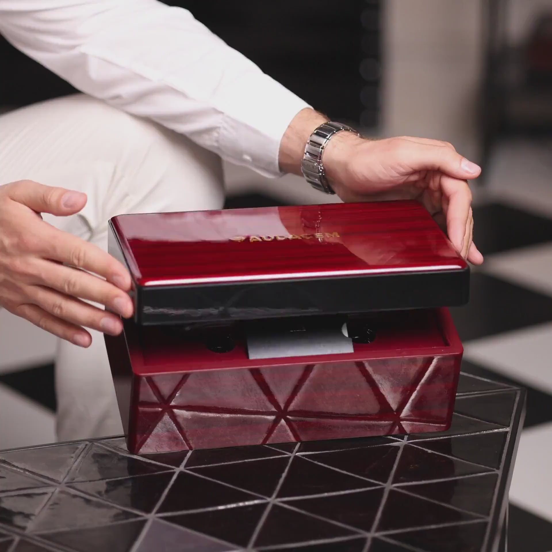Unboxing a luxurious red Audacem gift box with the Aequilibrium wine glass set, pouring red wine, and a couple toasting with handcrafted glasses on a black geometric table.